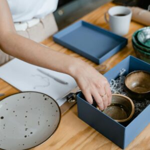 Person arranging handmade ceramic bowls in a box, preparing for store display.