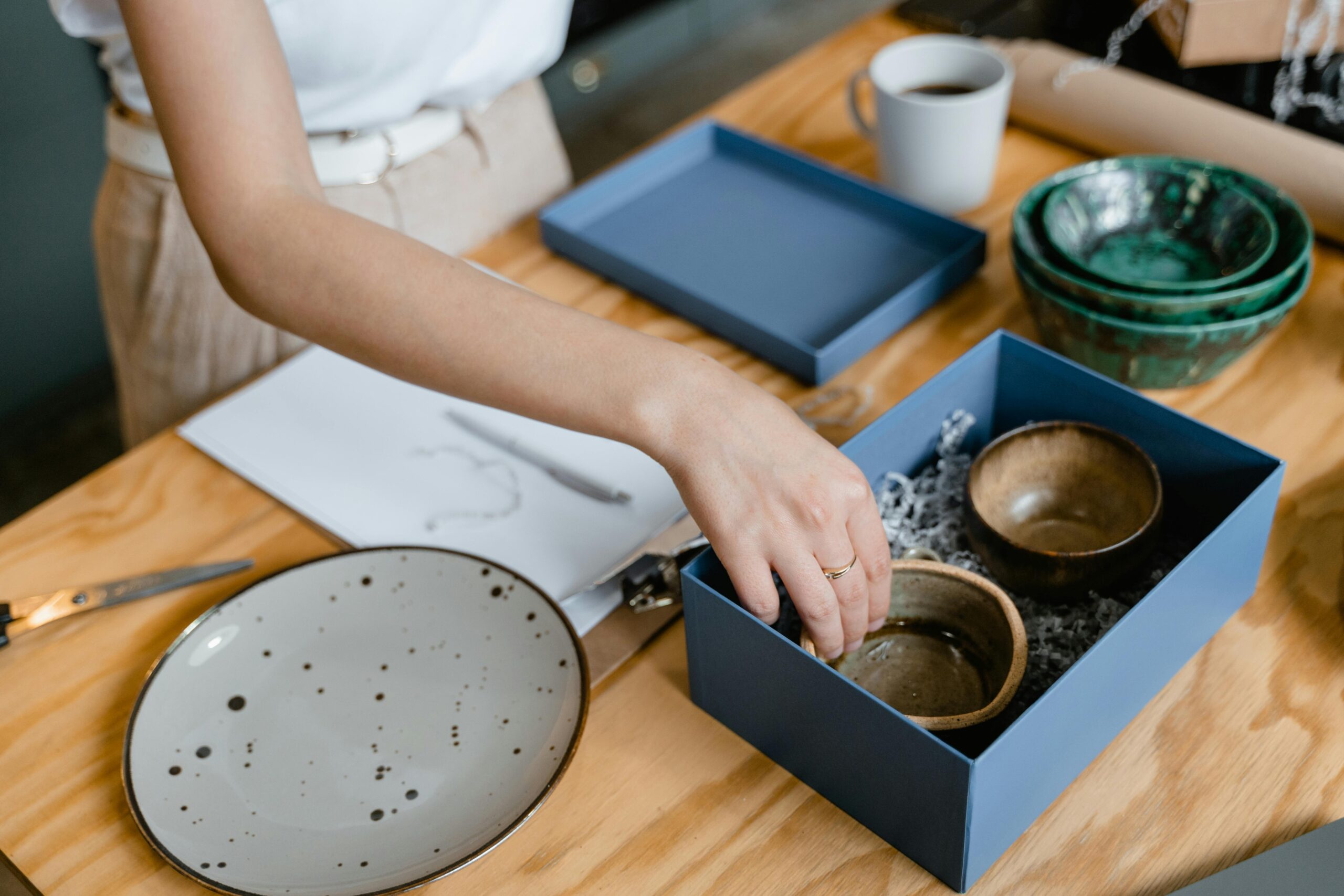 Person arranging handmade ceramic bowls in a box, preparing for store display.